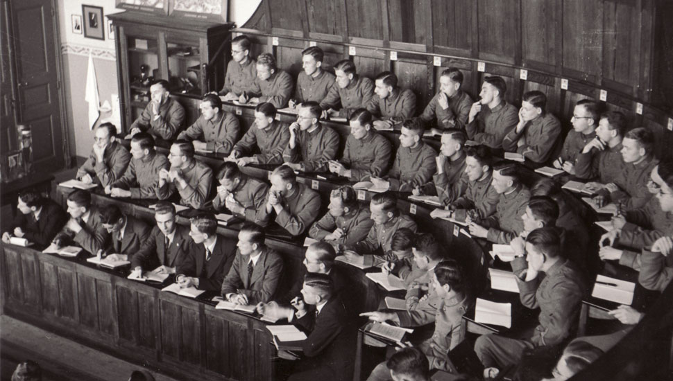 Gemobiliseerde studenten in Groningen, in uniform en op genummerde zitplaatsen, tijdens het college van de hoogleraar pathologie J.J.Th. Vos, eind 1939 of begin 1940. - Universiteitsmuseum Groningen